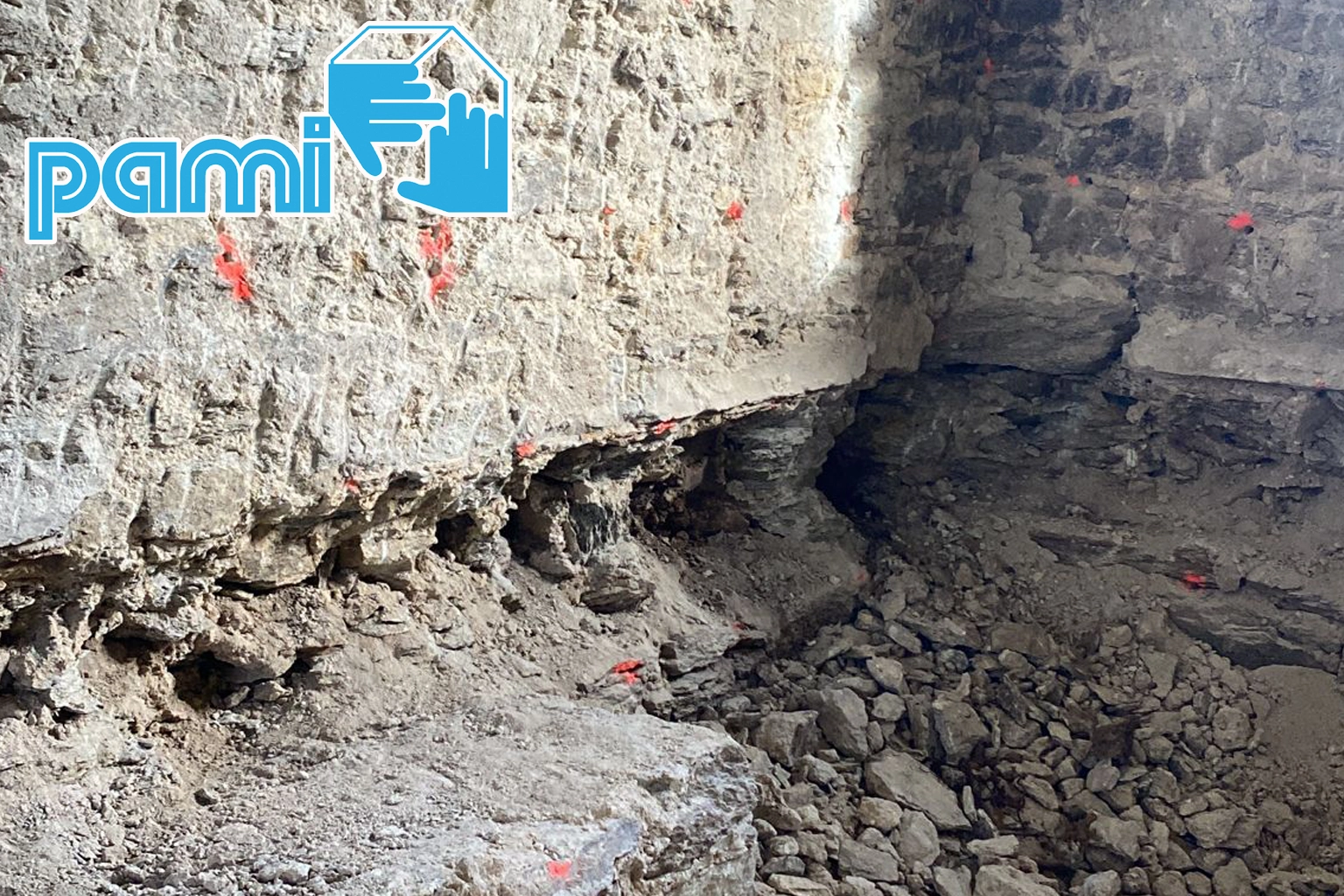 Mur décrouté et nettoyé sous un plancher, avec points de perçage tracés pour l’injection de fongicide après traitement des filaments de mérule à la flamme.